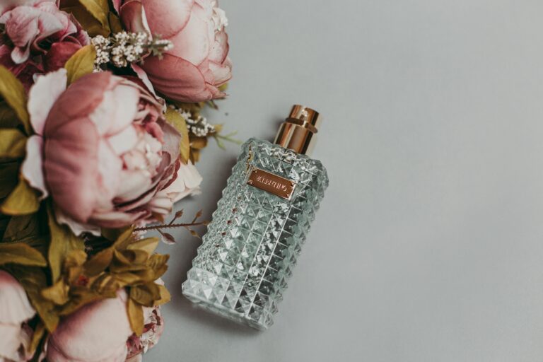 Tanie perfumy Śląsk w ozdobnym szklanym flakonie w otoczeniu różowych kwiatów.